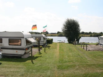 Quiet campsite near the water with caravans and flags in summer, surrounded by green nature.
