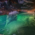 Besucherbergwerk "Marie Louise Stolln" Unterwasseraufnahme einer Höhle mit grünlich schimmerndem Wasser, Felsen und einer Leiter am Boden, beleuchtet von warmem Licht.Underwater shot of a cave with greenish shimmering water, rocks and a ladder at the bottom, illuminated by warm light.Podvodní záběr jeskyně se zelenavě se třpytící vodou, kameny a žebříkem na dně, osvětlený teplým světlem.Podwodne ujęcie jaskini z zielonkawo połyskującą wodą, skałami i drabiną na dnie, oświetlone ciepłym światłem.Onderwateropname van een grot met groenachtig glinsterend water, rotsen en een ladder op de bodem, verlicht door warm licht.Ripresa subacquea di una grotta con acqua scintillante verdastra, rocce e una scala sul fondo, illuminata da una luce calda.