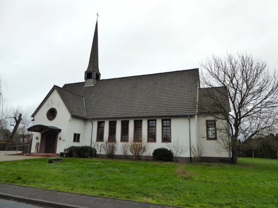 Ein kleines, weißes Kirchgebäude mit steilem, steinernem Turm und gepflegtem, grünem Rasen davor.
