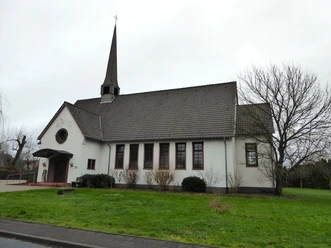 Kreuzkirche Herzebrock.JPG Ein kleines, weißes Kirchgebäude mit steilem, steinernem Turm und gepflegtem, grünem Rasen davor.