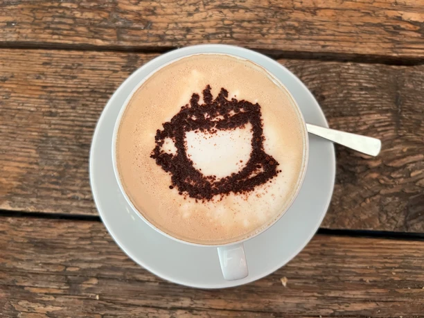 Cup of cappuccino with artfully speckled cocoa powder in the shape of a coffee cup on light crema.