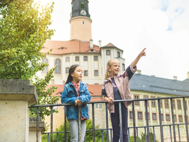 Dvě děti stojí na plotě před hradem Weesenstein a obdivují jeho architekturu.