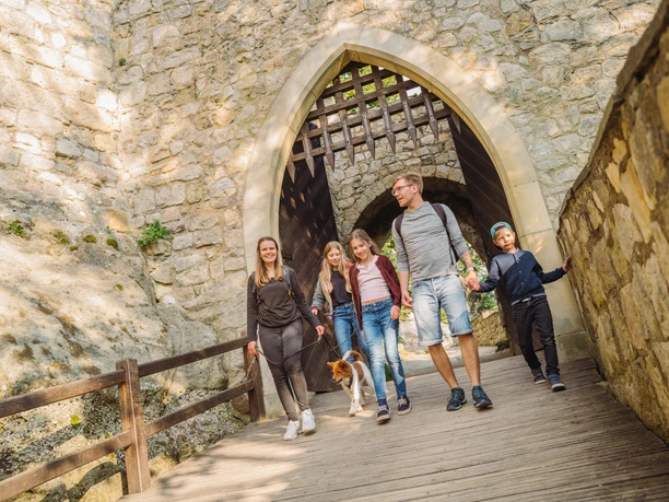 Burg Oybin Familie spaziert mit Hund durch den Torbogen der historischen Burg Oybin bei Sonnenschein.