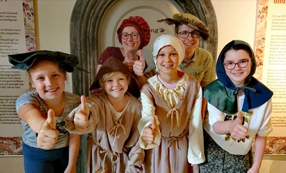 Museum Eine Gruppe in mittelalterlichen Kostümen vor einem historischen Museumseingang.