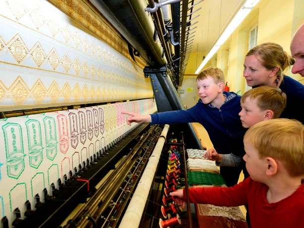 Schaustickerei Familie beobachtet fasziniert die detailreiche Arbeit einer historischen Stickmaschine.