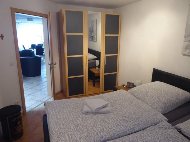 Fewo Strakeljahn Schlafzimmer Schlafzimmer mit Doppelbett, Kleiderschrank und Türöffnung zu einem hellen, gefliesten Wohnbereich.