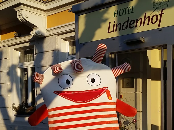 Sorgenfresser im Hotel Lindenhof in Bad Schandau Ein Plüschmonster mit Streifen, lachendem Gesicht und großen Augen posiert fröhlich vor dem Hotel.