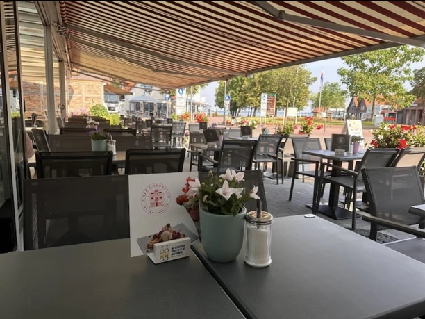 Sheltered terrace with blooming flowers and inviting atmosphere, tables and chairs under awnings.