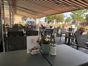 Terrasse Geschützte Terrasse mit blühenden Blumen und einladender Atmosphäre, Tische und Stühle unter Markisen.Sheltered terrace with blooming flowers and inviting atmosphere, tables and chairs under awnings.Overdækket terrasse med blomstrende blomster og indbydende atmosfære, borde og stole under markiser.Beschut terras met bloeiende bloemen en uitnodigende sfeer, tafels en stoelen onder luifels.