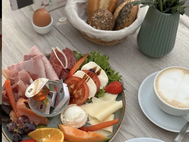 A richly laid breakfast plate with cold meats, cheese, bread, fresh fruit and cappuccino.