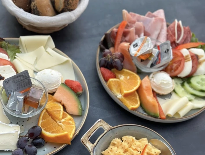 Ein reichhaltiger Frühstücksteller mit frischem Obst, verschiedenen Käsesorten und Rührei.