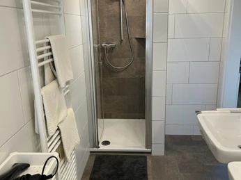 Fewo-Bad.jpg Barrierefreies Badezimmer mit bodengleicher Dusche, weiß gefliest, Handtuchheizkörper und Föhn.