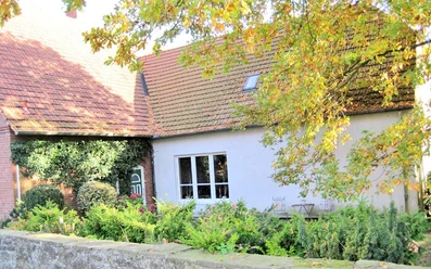 bildanzeige2.jpg Ein Haus mit roten Ziegeldächern, umgeben von grünen Sträuchern und herbstlich gefärbten Bäumen.