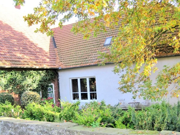 bildanzeige2.jpg Ein Haus mit roten Ziegeldächern, umgeben von grünen Sträuchern und herbstlich gefärbten Bäumen.