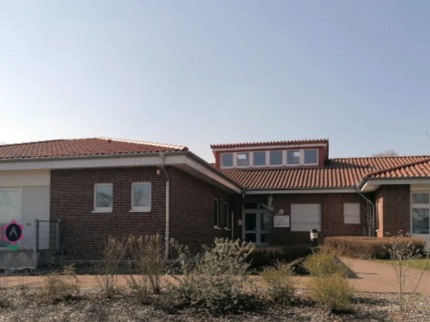 kindergarten_tausendfueßler_ahlsen_01.jpg Barrierefreier Eingangsbereich eines einstöckigen Ziegelgebäudes mit rotem Ziegeldach unter blauem Himmel.