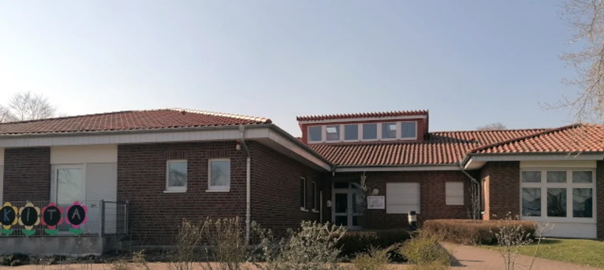 kindergarten_tausendfueßler_ahlsen_01.jpg Barrierefreier Eingangsbereich eines einstöckigen Ziegelgebäudes mit rotem Ziegeldach unter blauem Himmel.