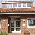 kindergarten_tausendfueßler_ahlsen.jpg Backsteinbau eines Kindergartens mit Fenstergiebel und dekorierter Eingangstür, umrahmt von Pflanzen.