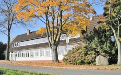 grundschule-ahlsen-reineberg.jpg Grundschule mit herbstlichen Bäumen, rotem Ziegeldach und weißem Anstrich an einer ruhigen Straße.