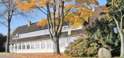 grundschule-ahlsen-reineberg.jpg Grundschule mit herbstlichen Bäumen, rotem Ziegeldach und weißem Anstrich an einer ruhigen Straße.