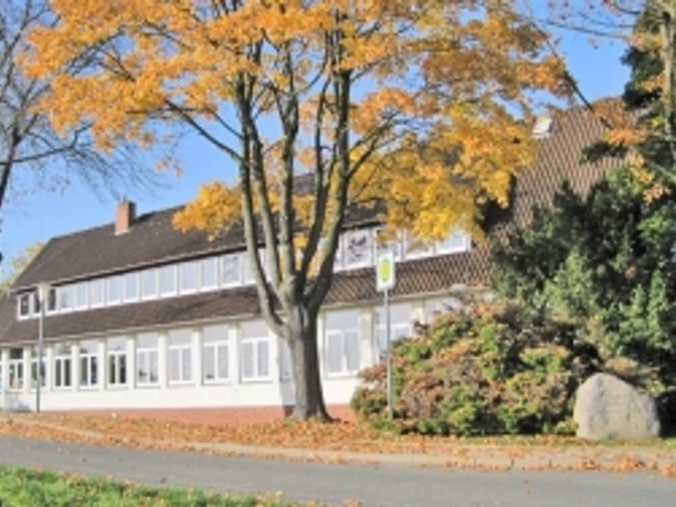 grundschule-ahlsen-reineberg.jpg Grundschule mit herbstlichen Bäumen, rotem Ziegeldach und weißem Anstrich an einer ruhigen Straße.