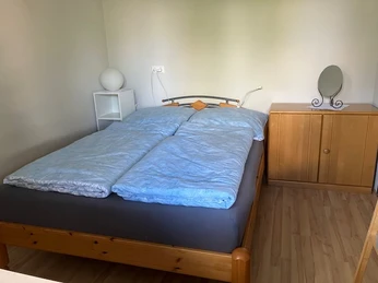 Ferienwohnung Ruhepol Helles Schlafzimmer in einer Ferienwohnung mit Doppelbett, Holzmöbeln und einem kleinen Spiegel.