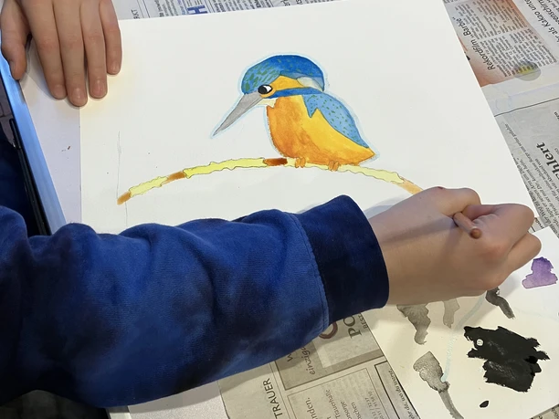 Aquarellmalen Ein Mensch malt mit Wasserfarben einen farbenfrohen Eisvogel auf einem Ast auf Zeichenpapier.