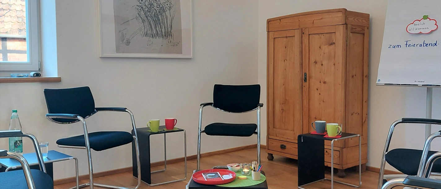 Feierabend_Dialog 2023_perspektiv katrinbusch_smt.jpg Meetingraum mit Holzboden, mehreren schwarzen Stühlen, einem Schrank und Flipchart, bereit für Diskussionen.