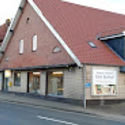 Bäckerei Harm Blumhoff, Gemeinde Rhauderfehn, Ostfriesland Eingang eines Gebäudes mit rotem Satteldach und mehreren Fenstern, an der Fassade ein Schild mit Text