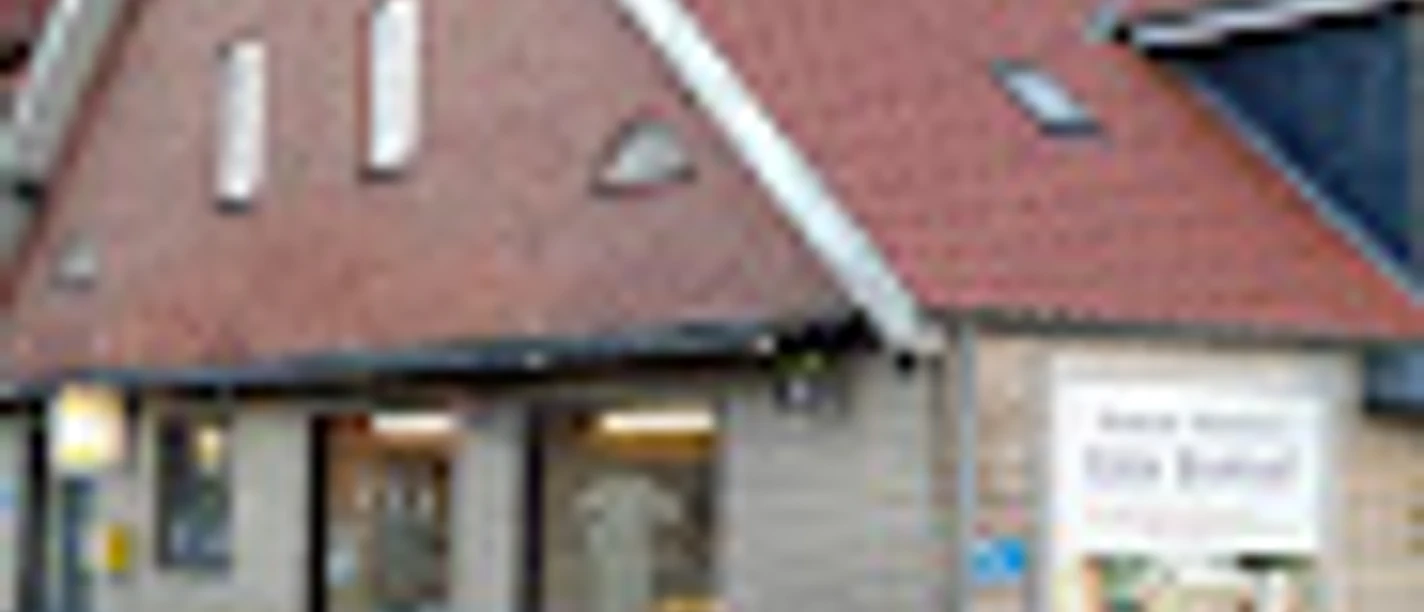 Bäckerei Harm Blumhoff, Gemeinde Rhauderfehn, Ostfriesland Eingang eines Gebäudes mit rotem Satteldach und mehreren Fenstern, an der Fassade ein Schild mit Text