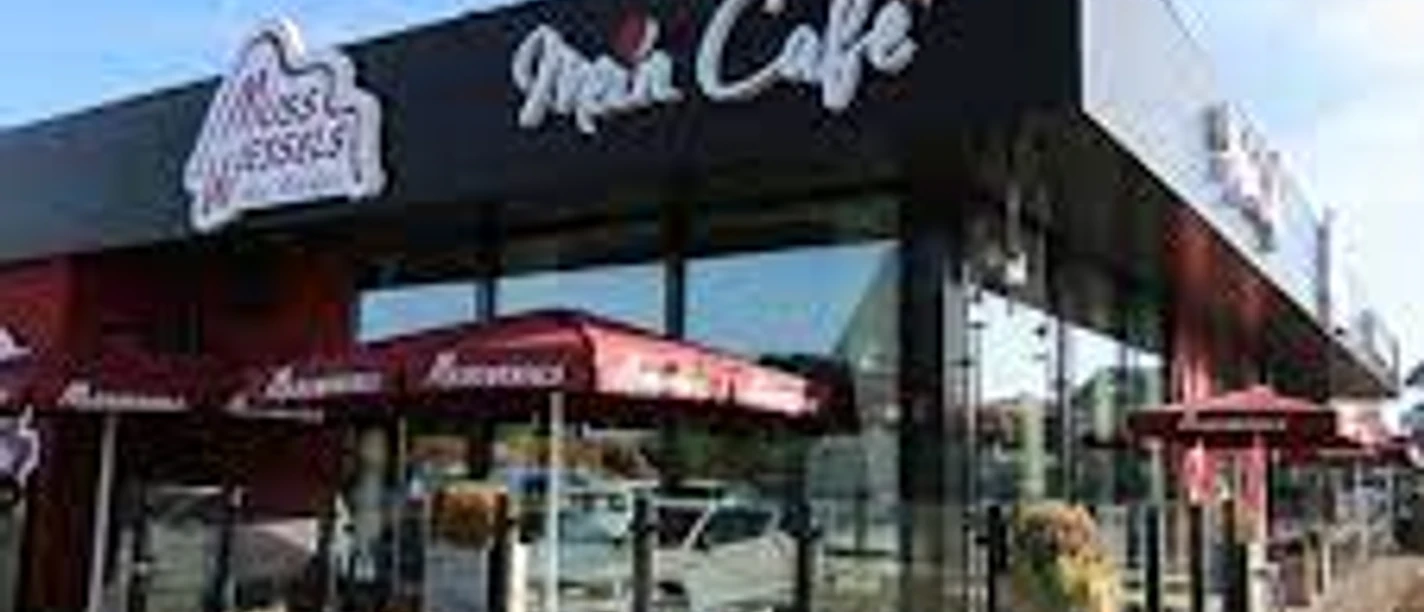 Bäckerei und Café Muss Wessels, Gemeinde Rhauderfehn, Ostfriesland Modernes Café mit schwarzer Fassade und roten Sonnenschirmen, Muss Wessels - Mein Café Schriftzug sichtbar