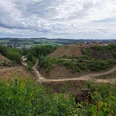 Steinbruch in Lindlar Steinbruch mit grünen Hügeln im Hintergrund, zahlreiche Baugeräte und wolkiger Himmel darüber.