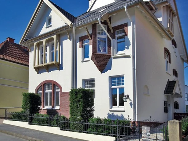 Außenansicht Ein zweistöckiges, helles Haus mit markanten roten Backsteinelementen und gepflegtem Vorgarten.