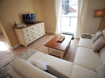 Wohnbereich Heller Wohnbereich mit cremefarbenem Sofa, Holz-Couchtisch und TV auf einer Kommode, Tageslicht durch Fenster.