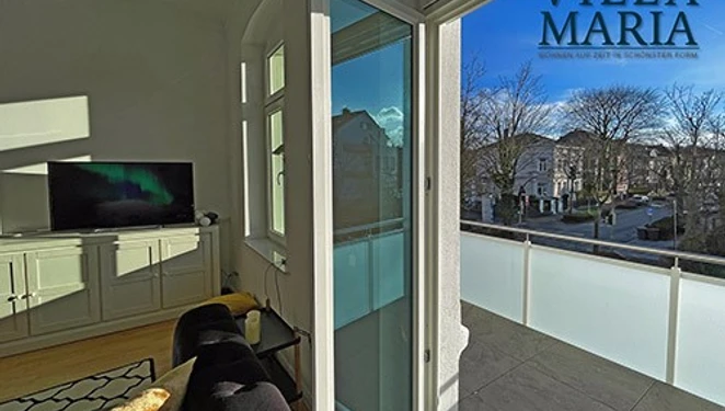 Balkon Blick aus Wohnbereich auf sonnendurchfluteten Balkon mit Aussicht auf ruhige, grüne Parkstraße.