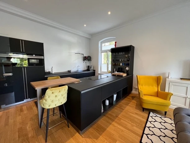 Küche Moderne Küche mit schwarzer Insel, Holzfußboden, gelbem Sessel und hohem Barhocker im Vordergrund.