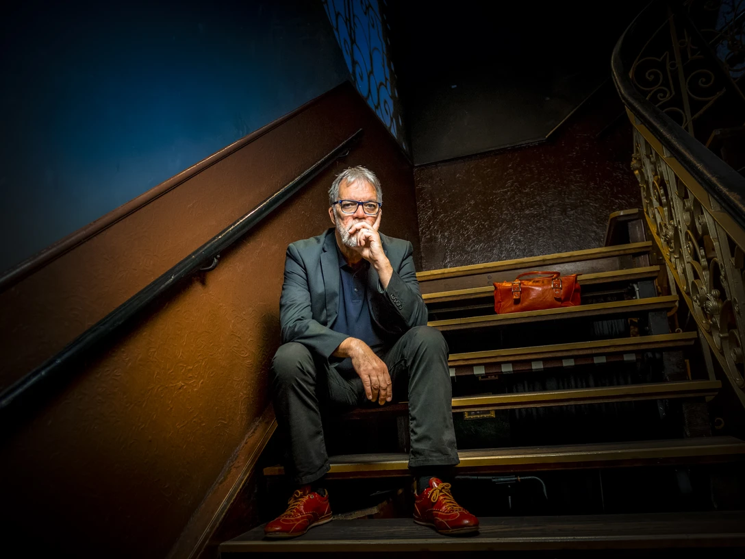 2018-08-30 WolfgangTrepper Foto Ingo Boelter.jpg Ein Mann sitzt nachdenklich auf einer Treppe, trägt rote Schuhe und ein dunkles Outfit.