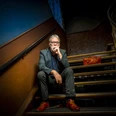 2018-08-30 WolfgangTrepper Foto Ingo Boelter.jpg Ein Mann sitzt nachdenklich auf einer Treppe, trägt rote Schuhe und ein dunkles Outfit.