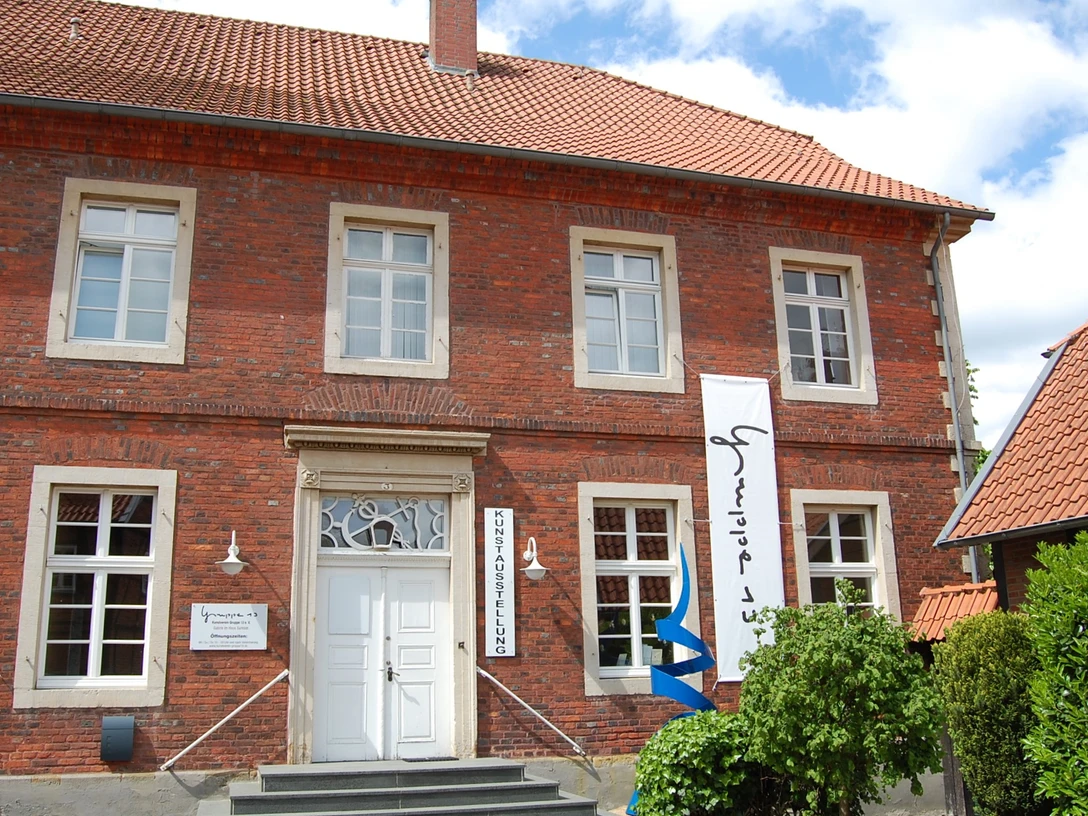 Galerie 13.jpg Historisches Gebäude aus rotem Backstein mit weißen Fenstern und Bannern am Eingang.