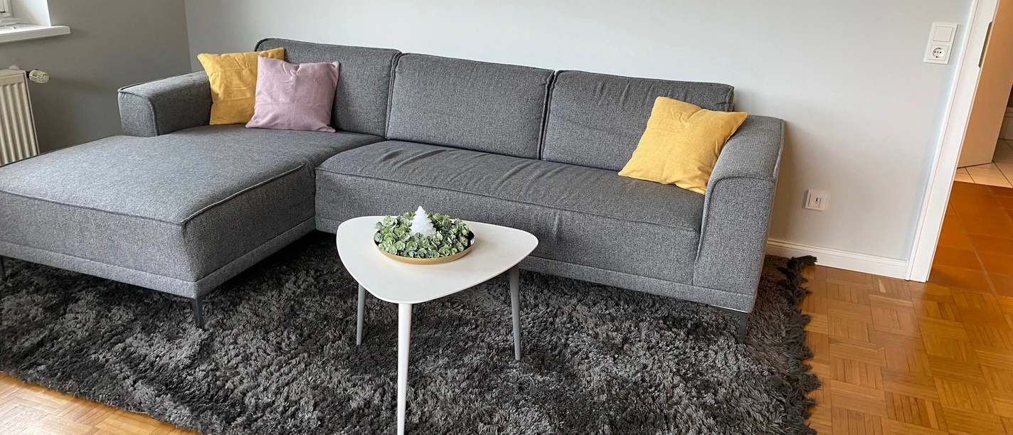 Ein modernes Wohnzimmer mit grauer Couch, bunten Kissen und einem weißen Couchtisch auf Teppich.