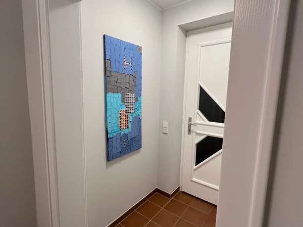 Flur mit hellem Wandanstrich, braunem Fliesenboden, moderner Kunst an der Wand und weiße Tür.