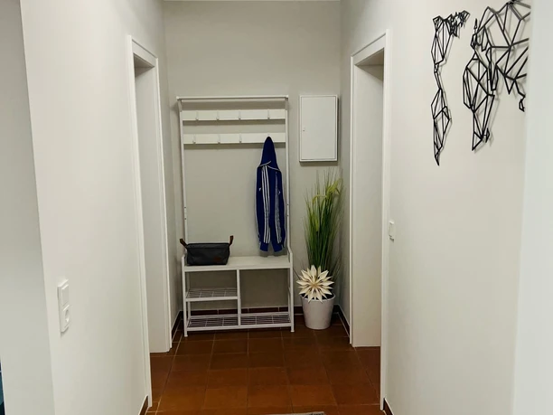 holsing3.jpg Langer Flur mit weißen Wänden, Garderobe, Pflanzen und moderner Weltkarte als Wanddeko.