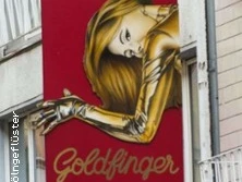 Ein auffälliges, rotes Schild mit einer goldenen Frau und dem Text "Goldfinger" in geschwungener Schrift.