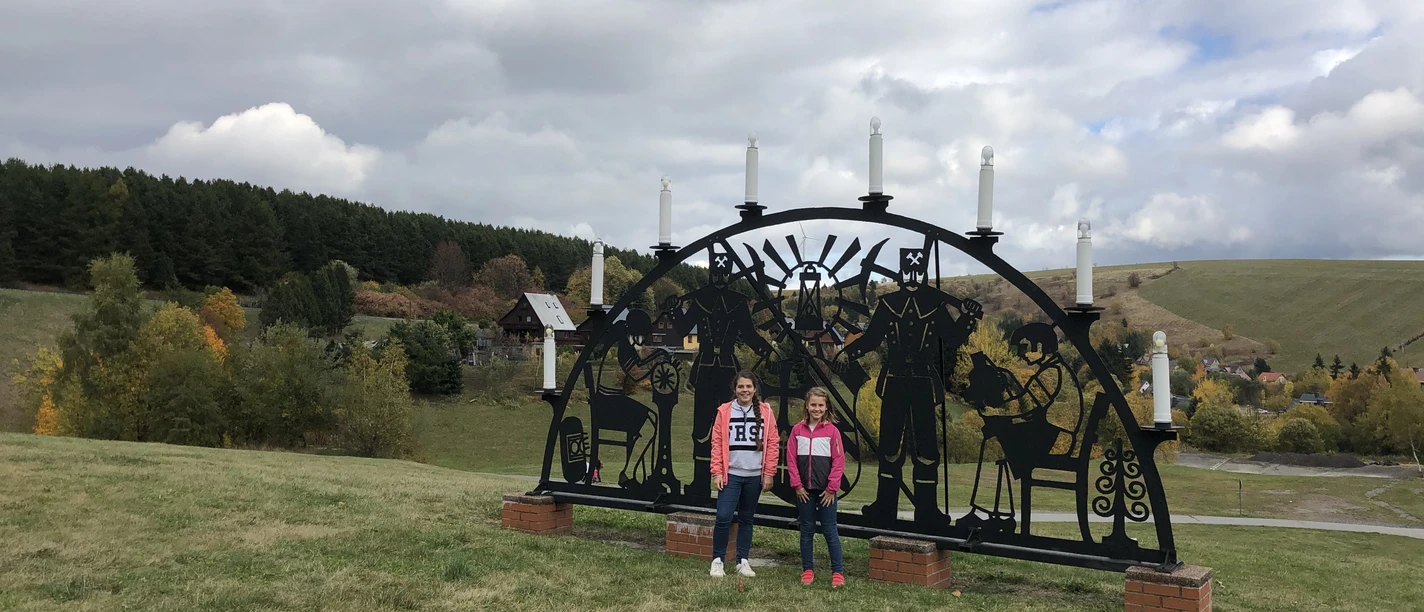im Erzgebirge Zwei Kinder stehen vor einem großen erzgebirgischen Lichterbogen auf einer Wiese.