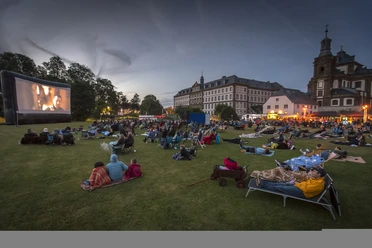 Bueren_Veranstaltungen_Open-Air-Kino_1 © Michael Kirchner.jpg Besucher genießen einen Filmabend im Freien, umgeben von historischen Gebäuden und abendlichem Licht.