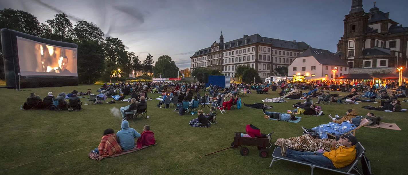 Bueren_Veranstaltungen_Open-Air-Kino_1 © Michael Kirchner.jpg Besucher genießen einen Filmabend im Freien, umgeben von historischen Gebäuden und abendlichem Licht.
