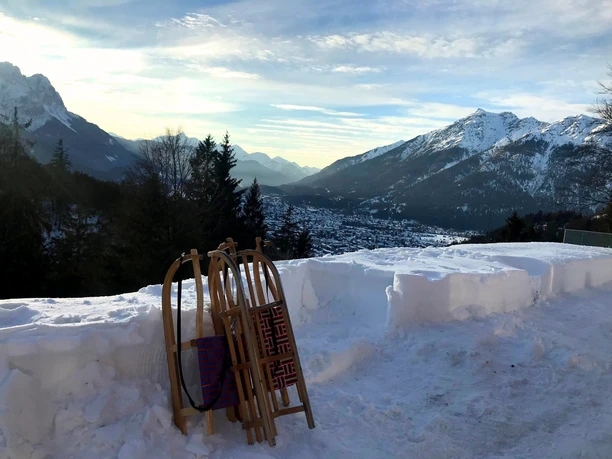 Blick von der Tannenhütte im Winter Holzschlitten lehnen im Schnee vor weitem Bergpanorama mit verschneiten Gipfeln und Tal
