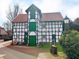 Fachwerkgebäude der Gutswassermühle Bad Holzhausen, umgeben von Bäumen und parkendem Auto.