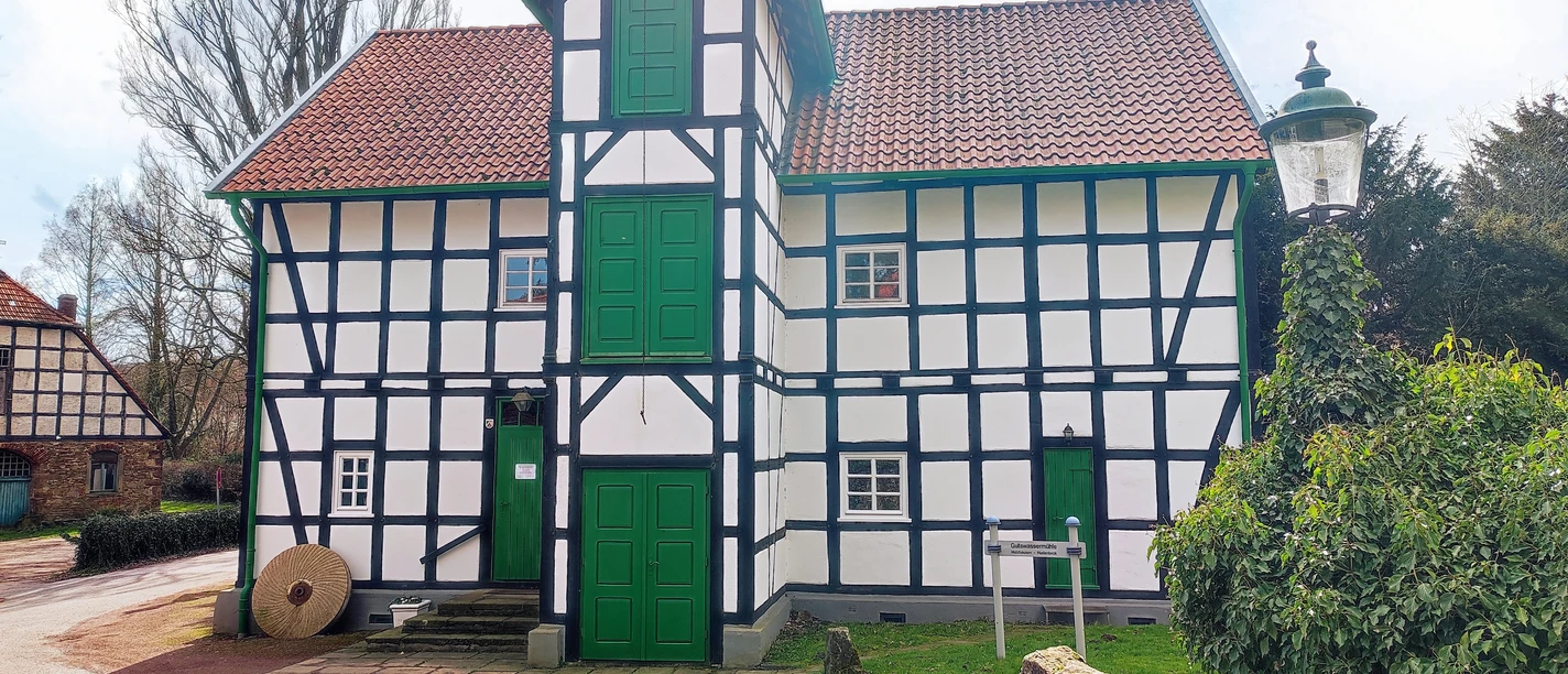 Gutswassermühle Bad Holzhausen Fachwerkgebäude der Gutswassermühle Bad Holzhausen, umgeben von Bäumen und parkendem Auto.