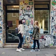 Belgisches Viertel Zwei Personen betrachten eine mit Stickern und Graffiti verzierte Wand in einer Stadtstraße.Two people look at a wall decorated with stickers and graffiti in a city street.