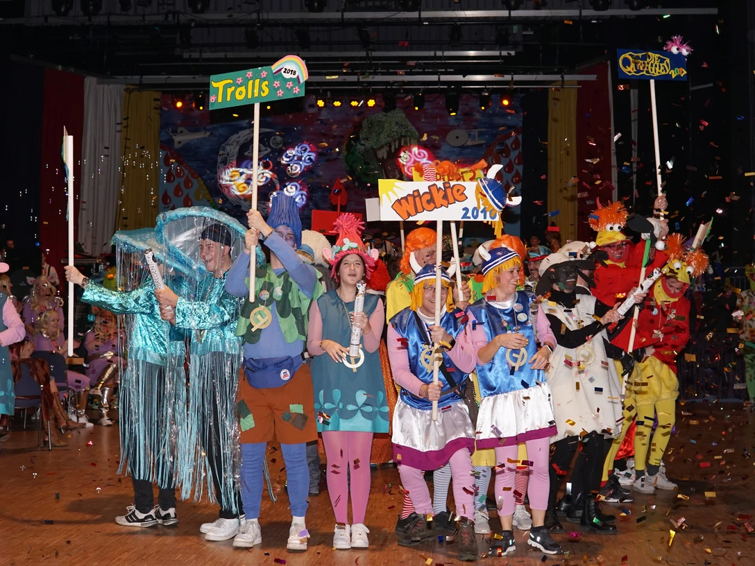 Maskenball Bild 1 - Katja Tevs.jpg Menschen in bunten Kostümen beim Maskenball mit farbenfrohem Konfetti und festlicher Dekoration.